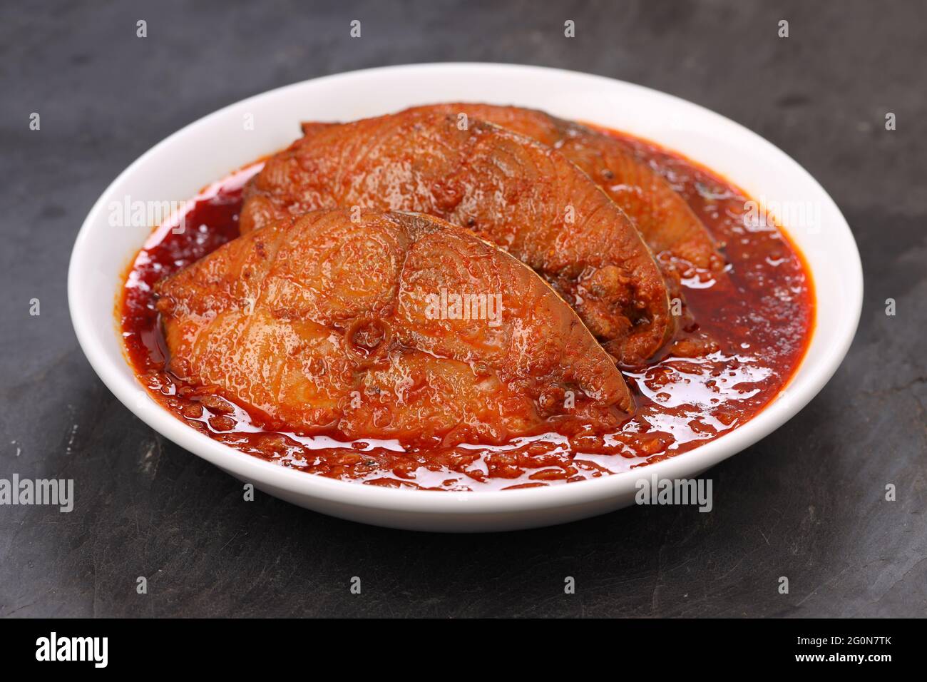 Séer curry de poisson, curry traditionnel de poisson indien, arrangé dans un bol en céramique blanc sur un fond gris texturé, isolé. Banque D'Images