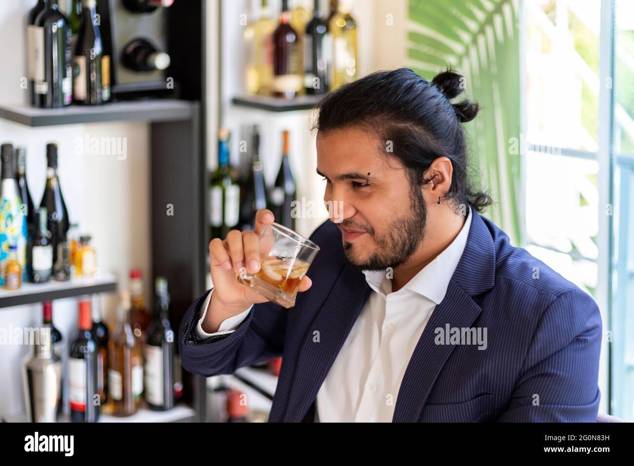 jeune latino homme assis sur le cabinet de la maison, boissons whisky. Nouvelle normale. Banque D'Images