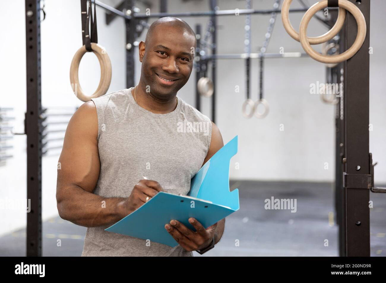 Entraîneur personnel noir dans le centre de fitness. Il sourit et prend des notes dans un bloc-notes. Espace pour le texte. Banque D'Images