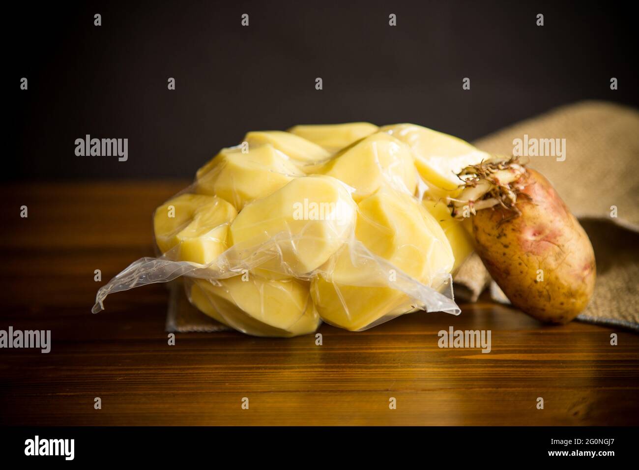 pommes de terre pelées fermées dans un sac à vide et vieilles pommes de terre germées sur une table en bois Banque D'Images