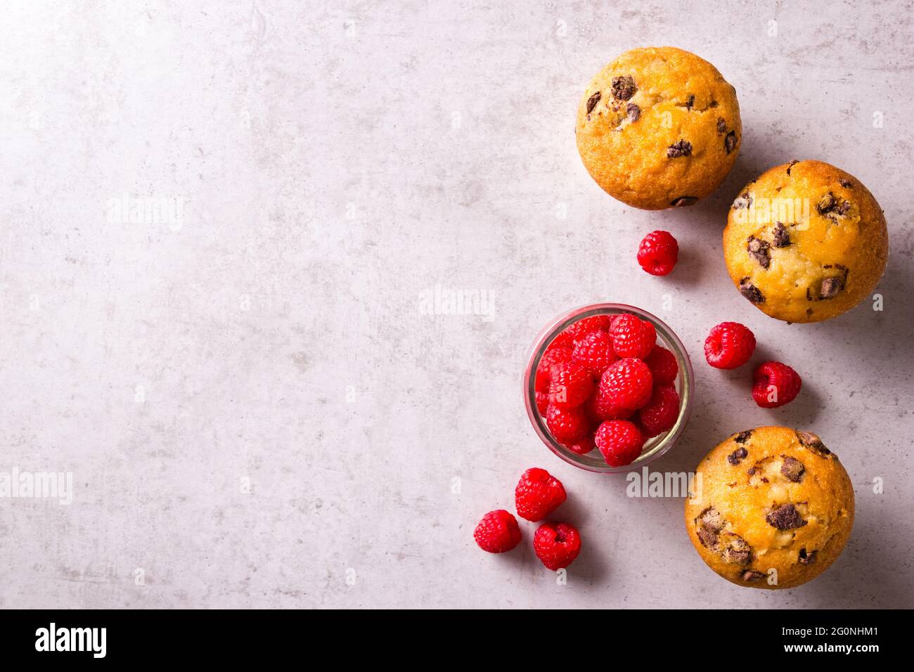 Cupcakes dorés fraîchement cuits et framboises rouges fraîches dans un pot sur comptoir gris clair Banque D'Images