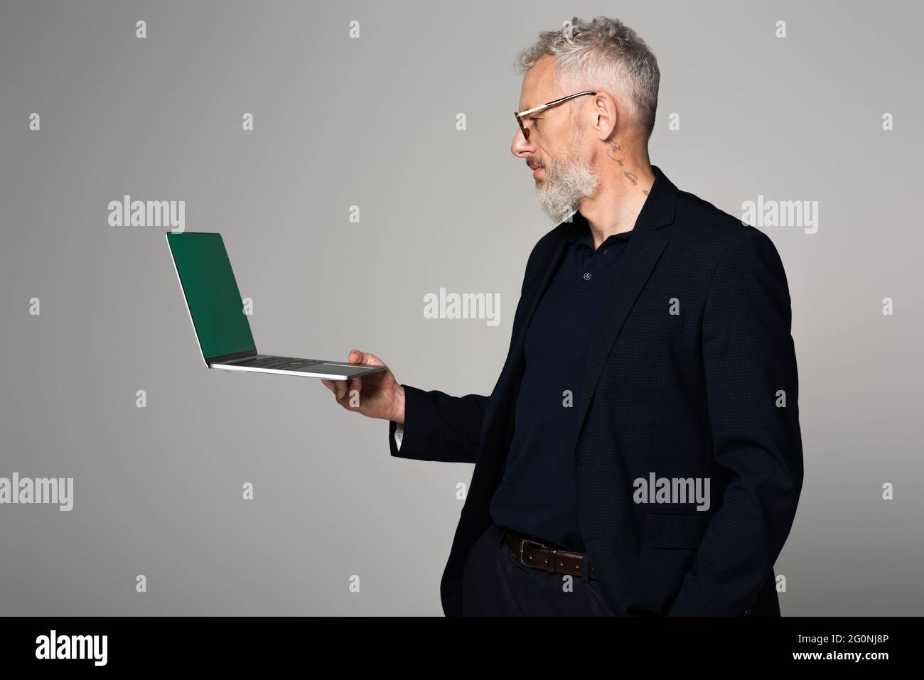 tatoué homme d'âge moyen dans des lunettes regardant l'ordinateur portable isolé sur gris Banque D'Images