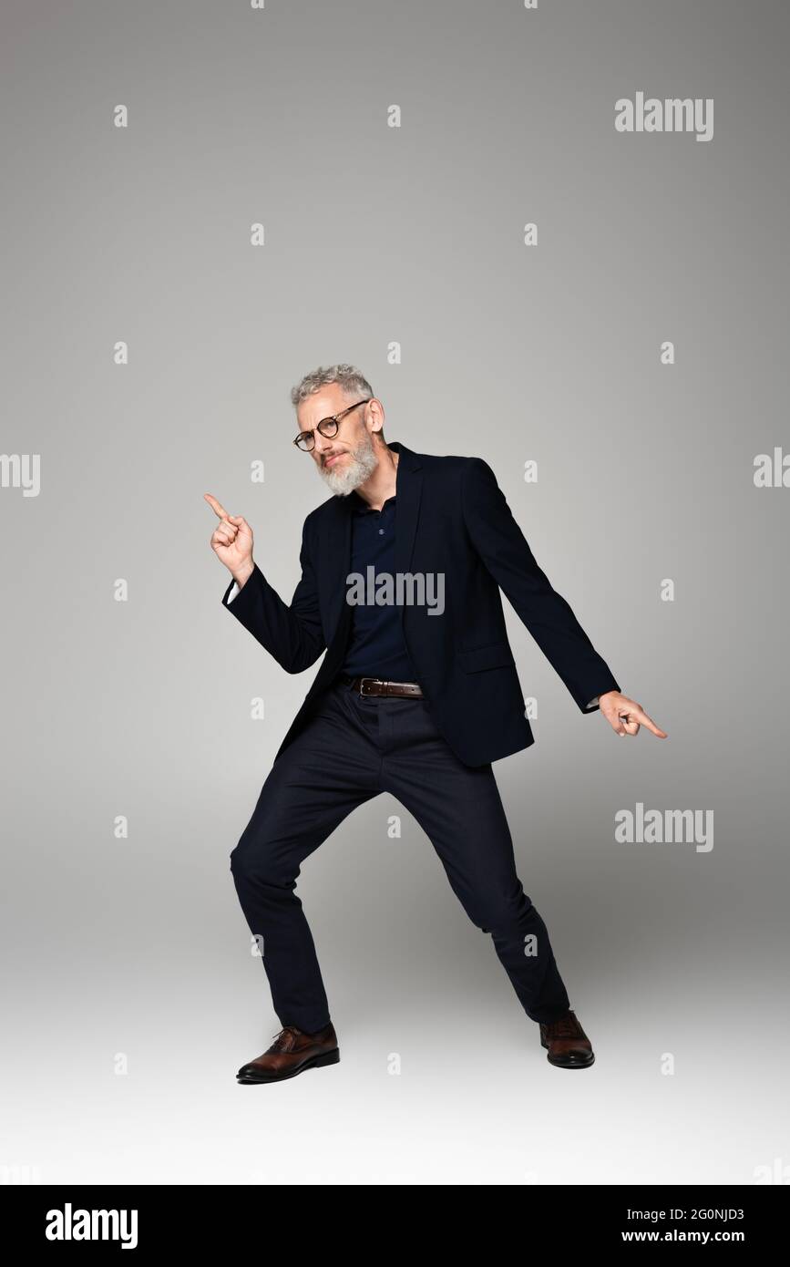 homme d'âge moyen en lunettes et costume dansant sur le gris Banque D'Images