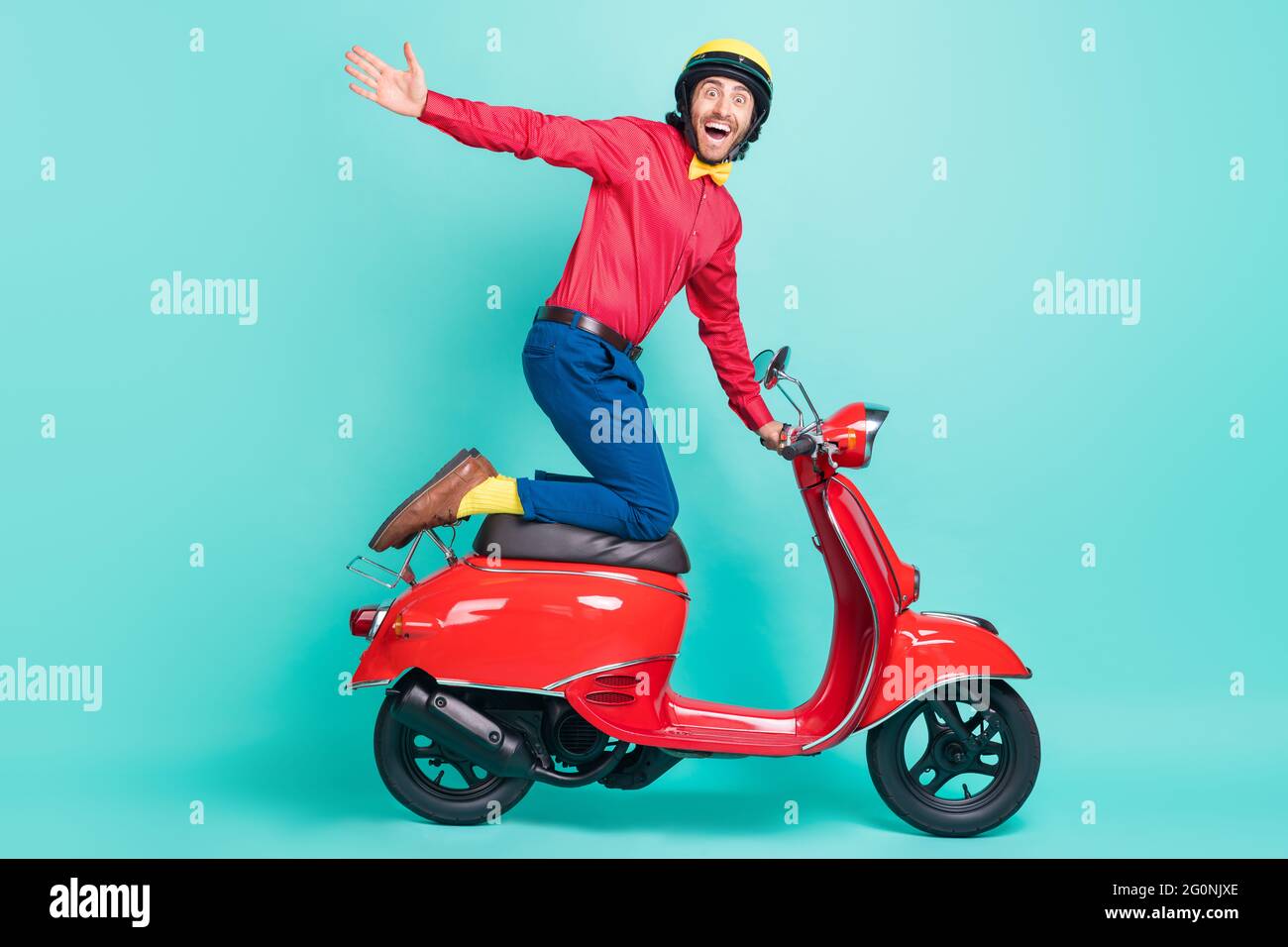 Photo de côté pleine taille de profil de funky souriant extrême jeune homme à la vitesse rapide mobylette isolée sur fond de couleur sarcelle Banque D'Images