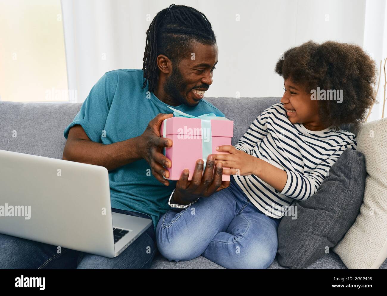 Le père afro-américain donne à sa fille un cadeau d'anniversaire qu'il a commandé sur Internet à partir de son ordinateur portable. Papa positif communique avec son enfant, Banque D'Images