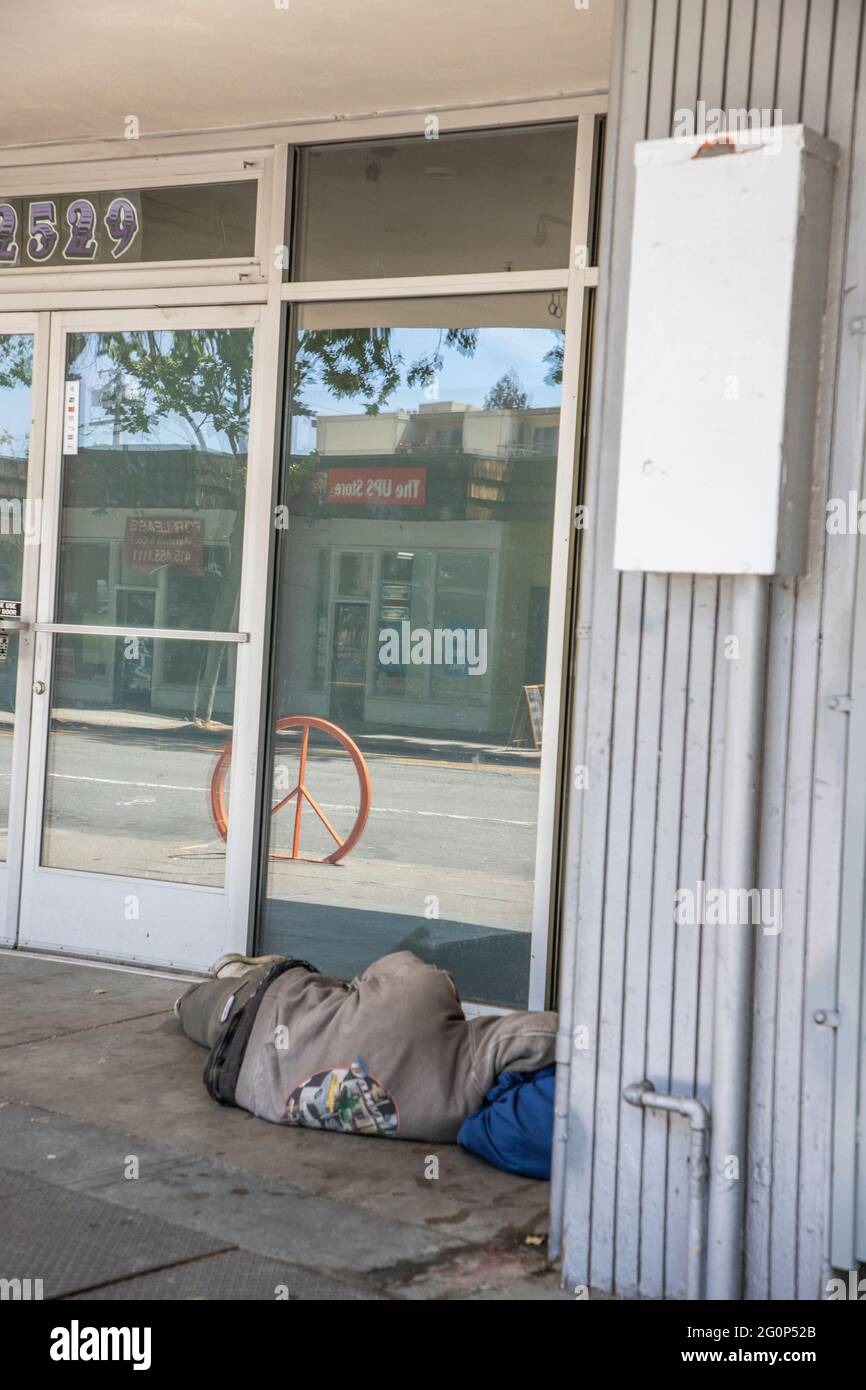 Homme sans domicile prenant une sieste devant une vitrine vide sur Telegraph Ave. À Berkeley, Californie. Le panneau de la paix de Berkeley se reflète dans la fenêtre pour Banque D'Images