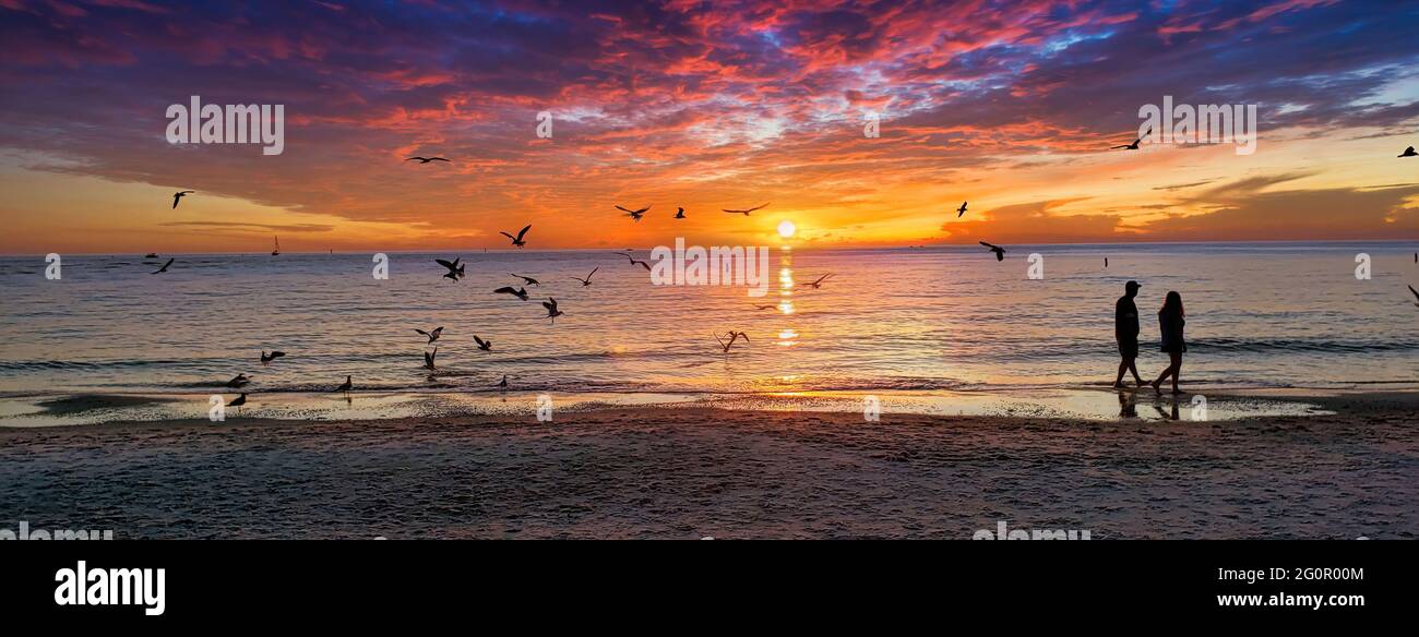Une belle photo de paysage de coucher de soleil avec une silhouette d'un couple marchant le long de la rive. Banque D'Images