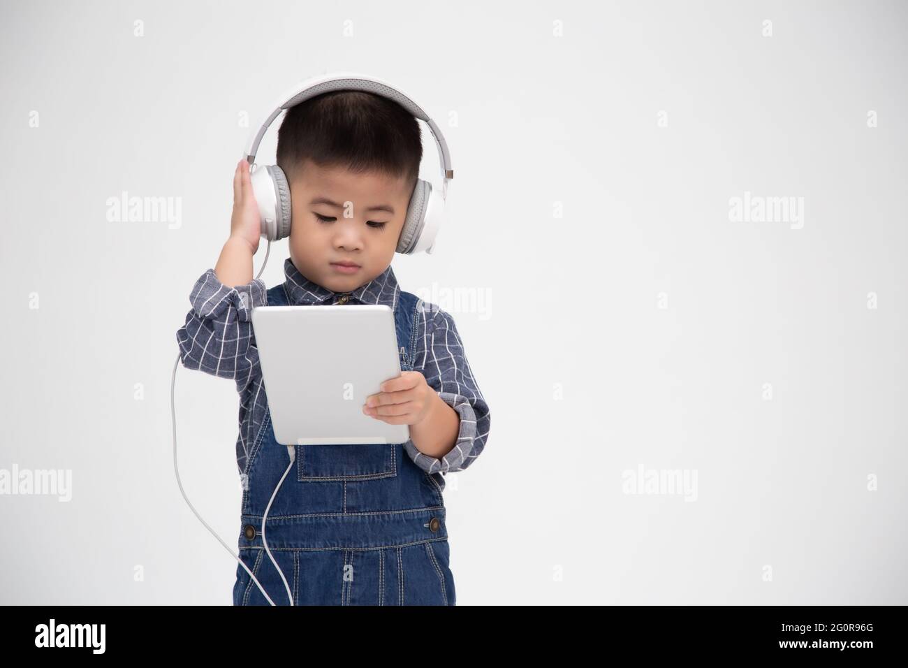 Portrait d'un petit enfant mignon satisfait tenant une tablette et écoutez de la musique sur une application isolée sur fond blanc Banque D'Images