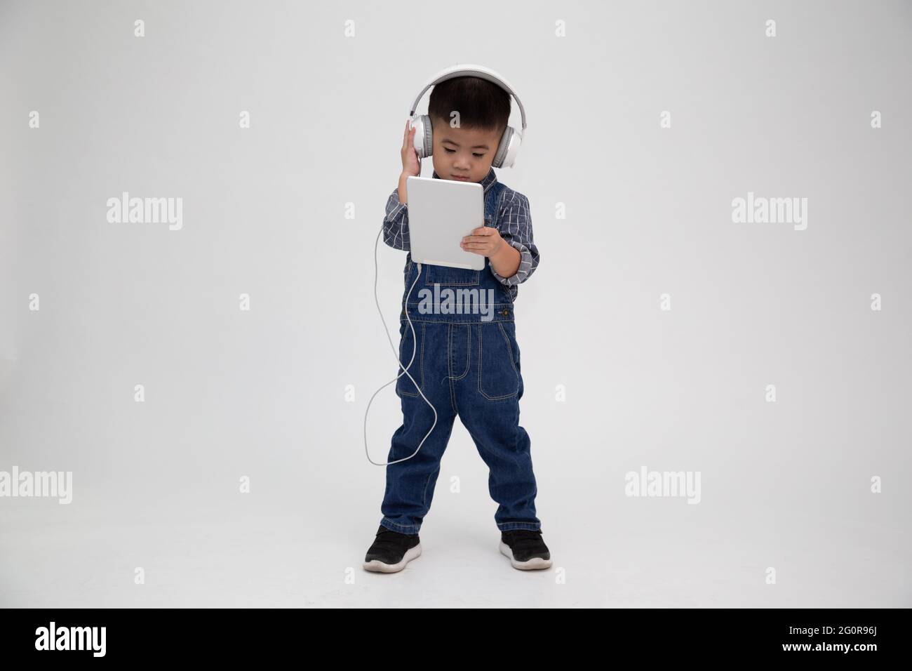 Portrait d'un petit enfant mignon satisfait tenant une tablette et écoutez de la musique sur une application isolée sur fond blanc Banque D'Images