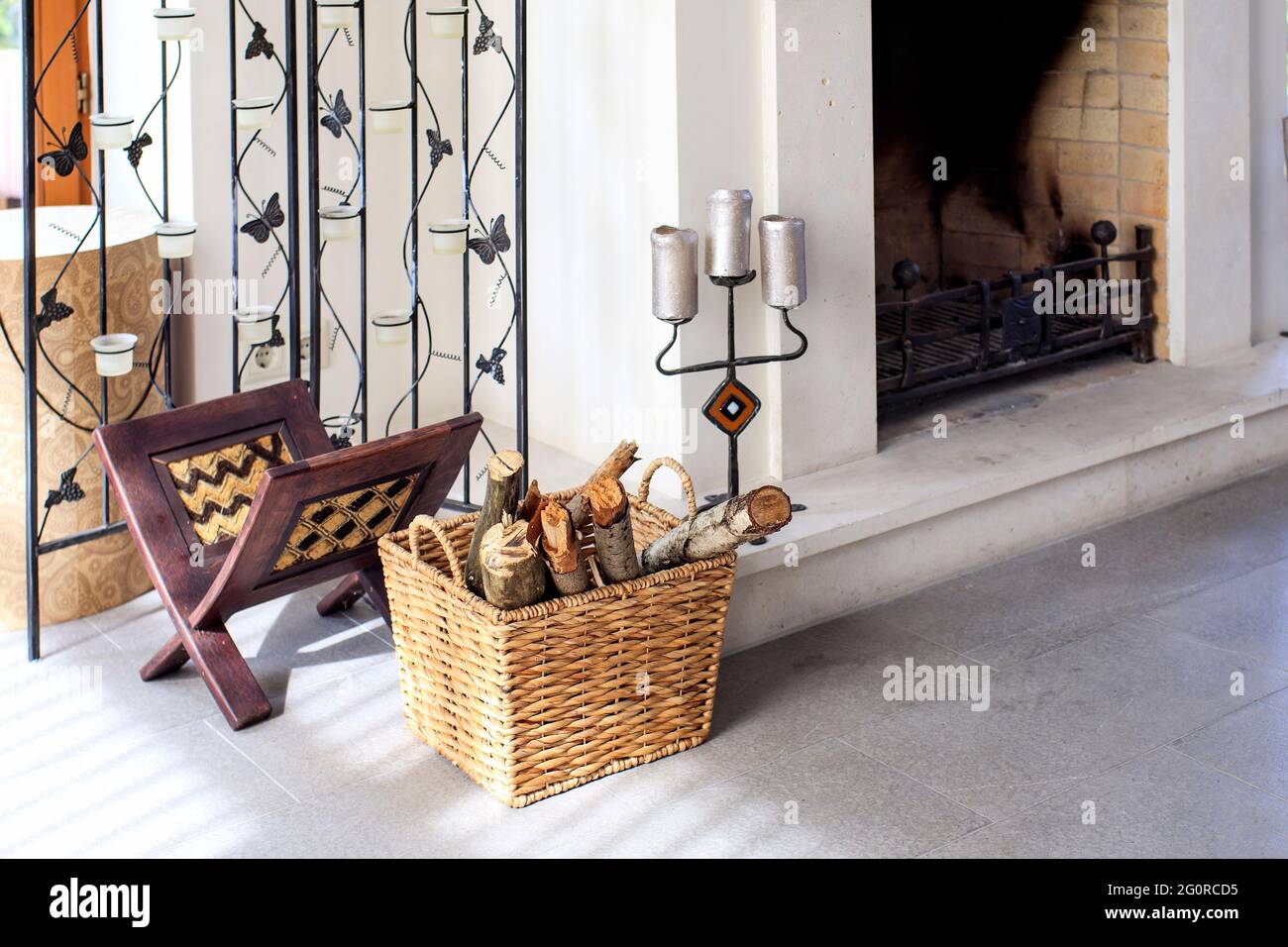 Fragment d'une cheminée avec un panier en osier avec bois de chauffage, un stand pour les magazines et les bougies dans un chandelier. Agrément Banque D'Images