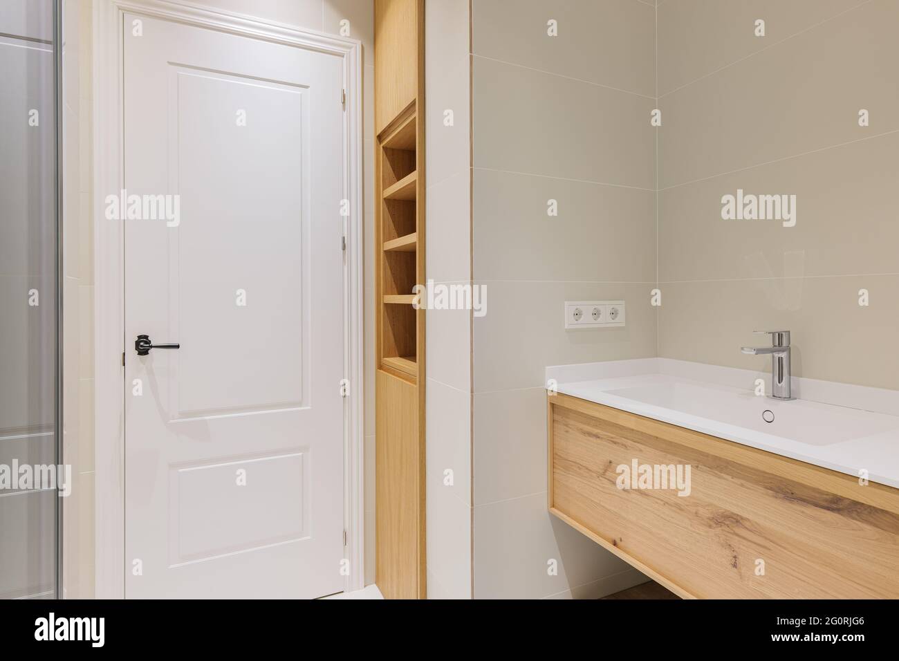 Salle de bains moderne avec base en bois pour lavabo blanc, carrelage clair. Mobilier en bois intégré avec étagères. Banque D'Images