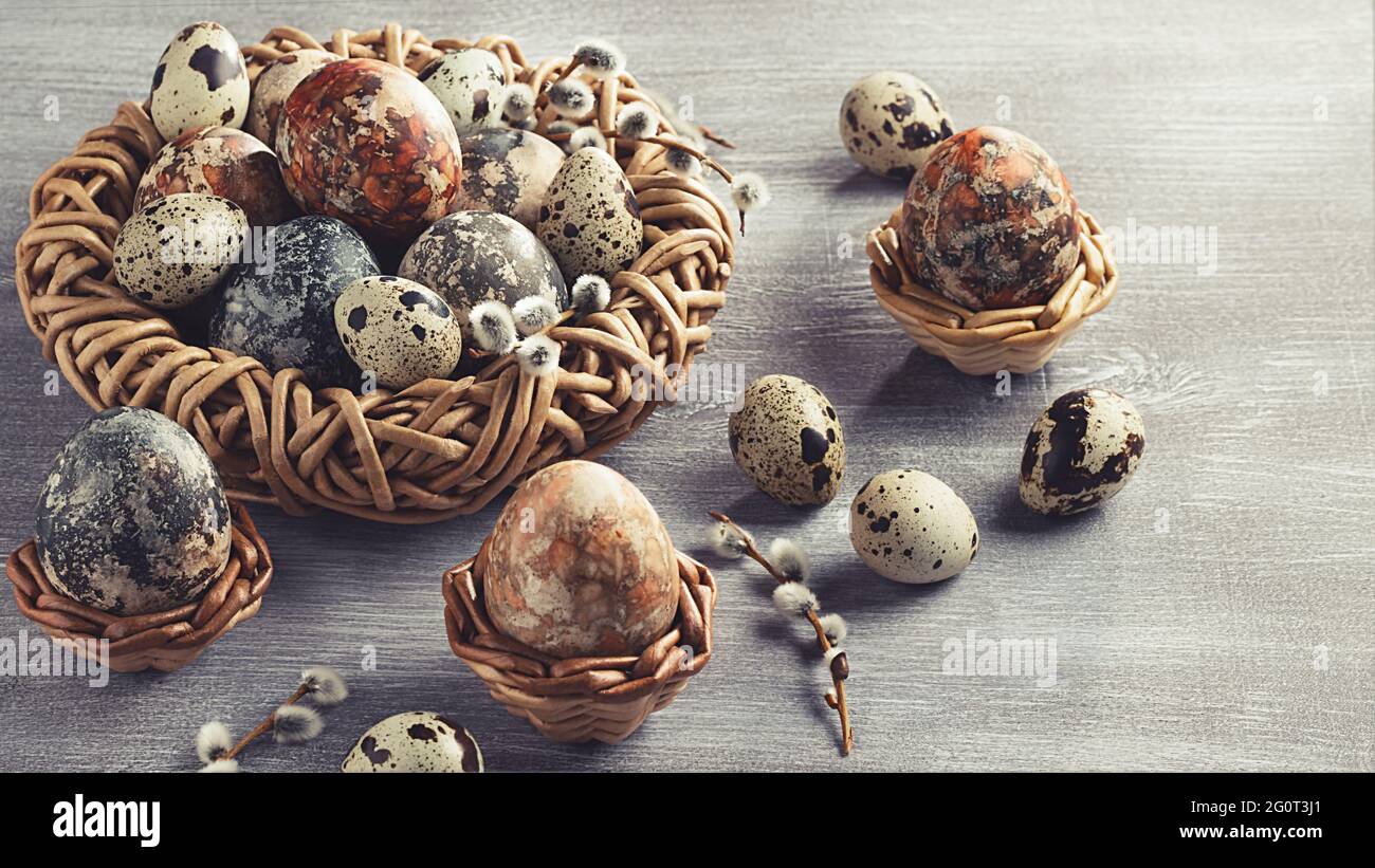 Composition de Pâques - plusieurs oeufs en marbre peints avec des teintures naturelles dans un nid en osier et des paniers. Banque D'Images