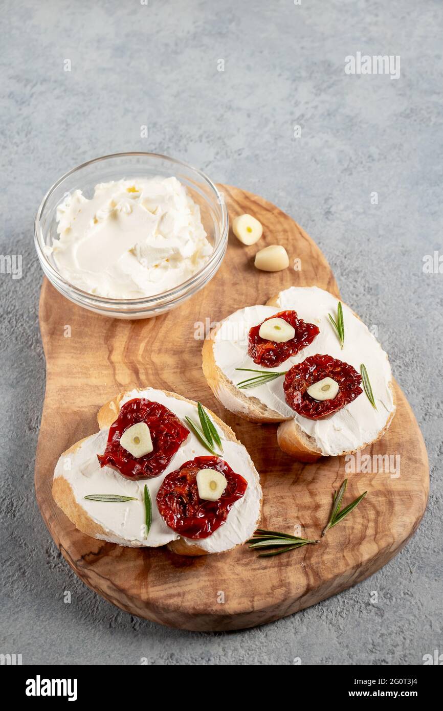 Sandwichs maison avec fromage à la crème et tomates séchées sur un plateau d'olives en bois - délicieux petit déjeuner sain, cuisine italienne, image verticale Banque D'Images