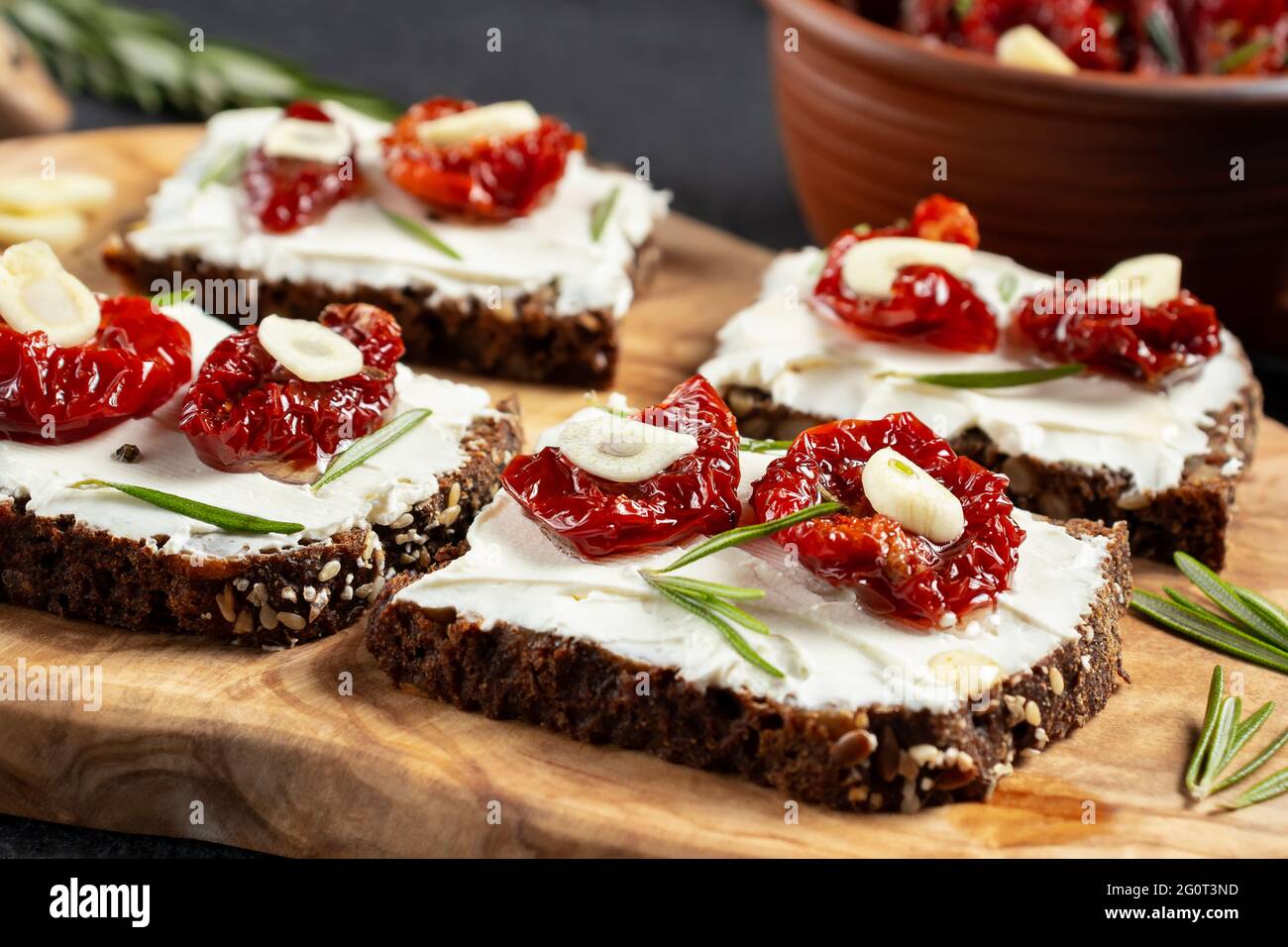 Petits-sandwiches multigrains faits maison avec fromage à la crème et tomates séchées sur un plateau en bois, gros plan. Concept de saine alimentation Banque D'Images