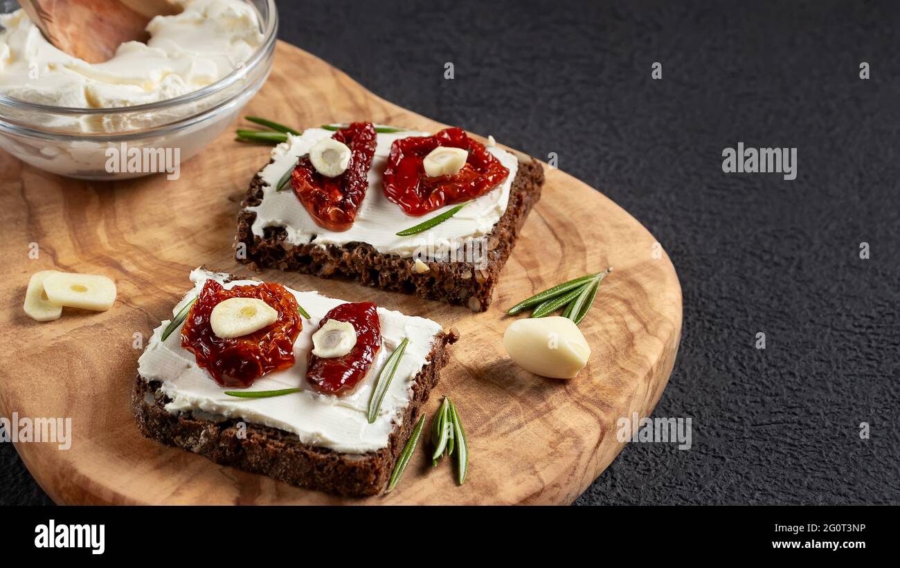 Des sandwichs au pain multigrain faits maison avec fromage à la crème et tomates séchées sur un plateau en bois. Concept de saine alimentation, copier l'espace. Banque D'Images