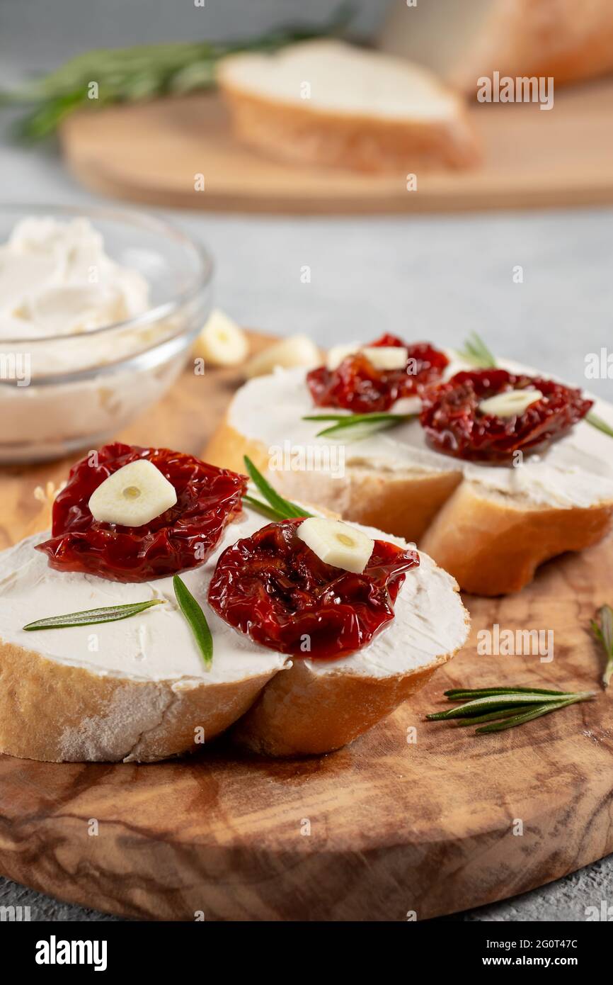 Sandwichs maison avec fromage à la crème et tomates séchées sur un plateau d'olives en bois - délicieux petit déjeuner sain, cuisine italienne, image verticale Banque D'Images