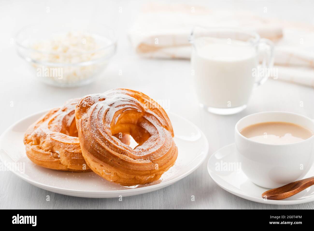 Café du matin avec gâteau. Rondelles de crème anglaise, café, crème, fromage cottage sur une table en bois blanc. Banque D'Images