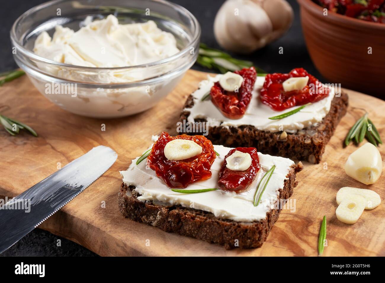 Petits-sandwiches multigrains faits maison avec fromage à la crème et tomates séchées sur un plateau en bois, gros plan. Concept de saine alimentation. Banque D'Images