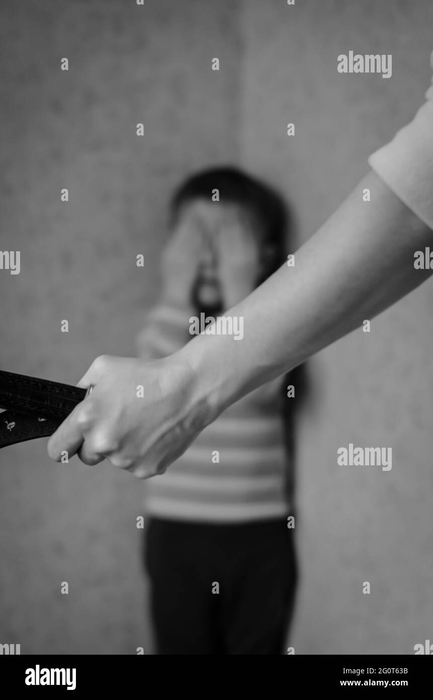 Maman avec une ceinture se tient devant l'enfant. Le fils pleure dans le coin. Violence domestique contre les enfants. Banque D'Images
