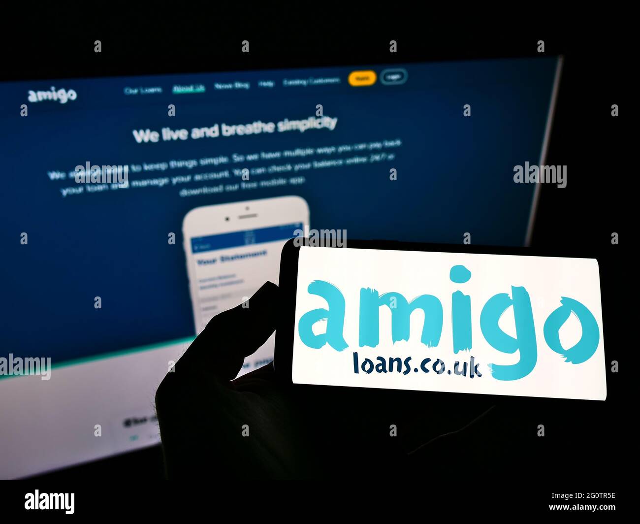 Personne tenant un téléphone portable avec le logo du garant de prêt britannique Amigo Holdings PLC à l'écran en face de la page Web d'affaires. Mise au point sur l'affichage du téléphone. Banque D'Images