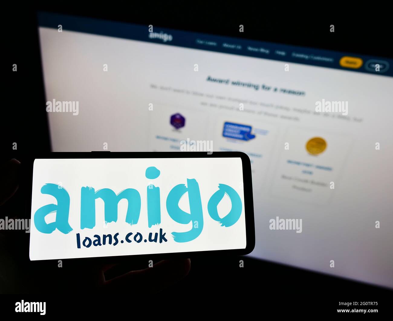Personne tenant le téléphone portable avec le logo d'affaires du garant de prêt britannique Amigo Holdings PLC à l'écran en face de la page web. Mise au point sur l'affichage du téléphone. Banque D'Images