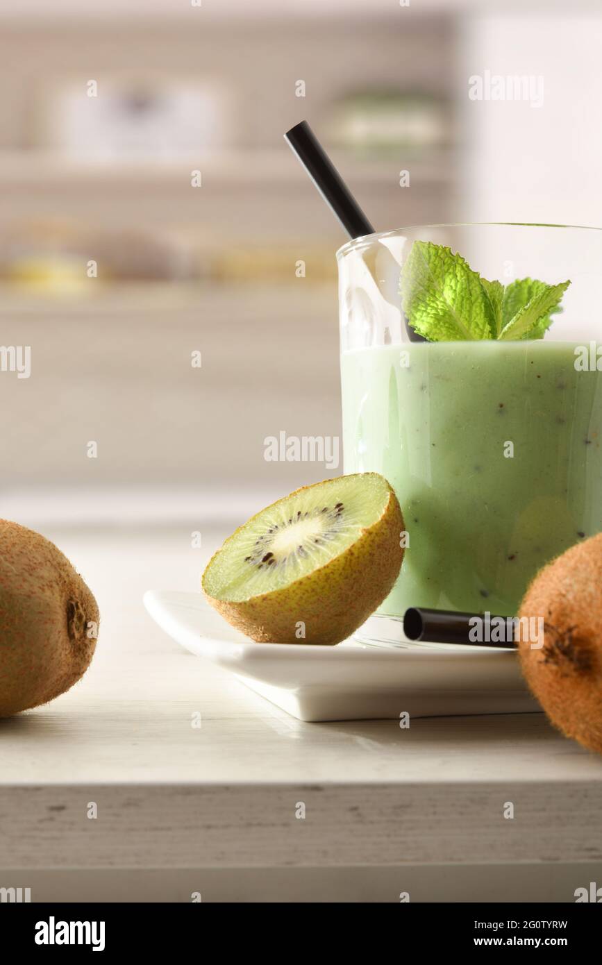 Un verre de boisson au kiwi et un contenant coupent les fruits sur le banc de cuisine de près. Vue avant. Composition verticale. Banque D'Images
