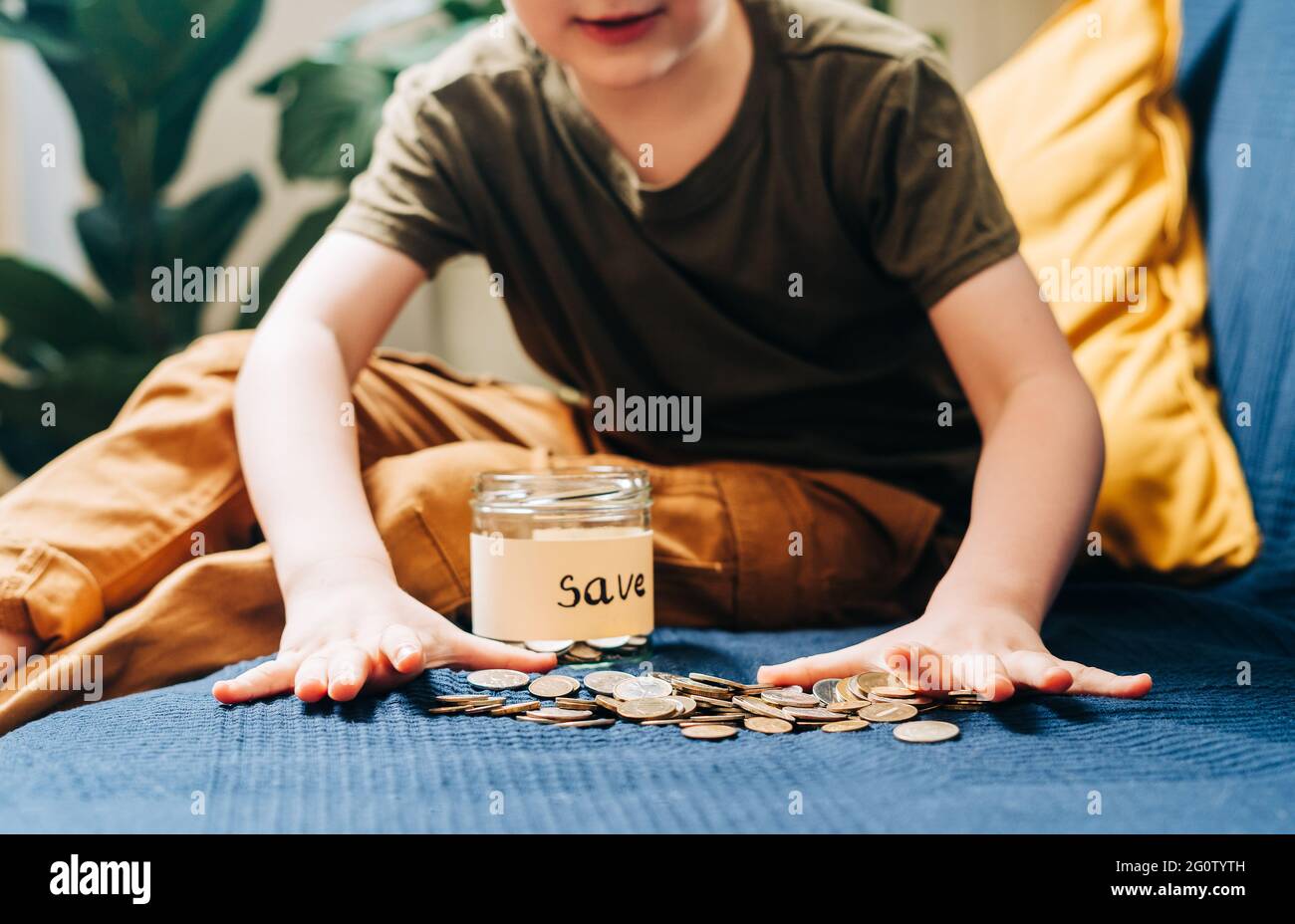 Gros plan sur les mains de petit enfant garçon qui attrapant et mettant des pièces de monnaie empilées dans un pot en verre avec une étiquette de sauvegarde. Don, économie d'argent, charité, famille Banque D'Images