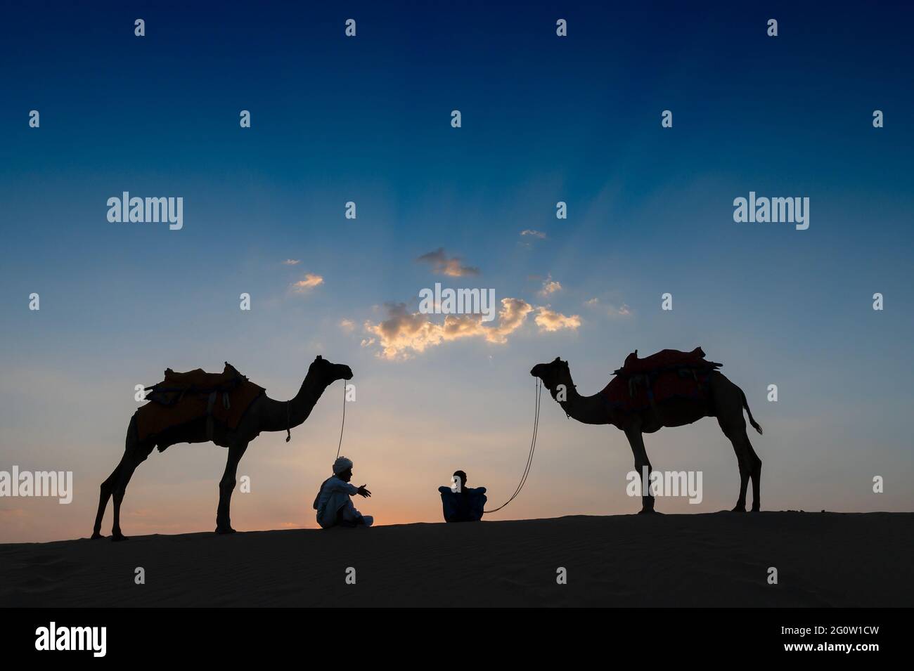 Silhouette de deux caméléers et de leurs chameaux sur les dunes de sable du désert de Thar, Rajasthan, Inde. Coucher de soleil en arrière-plan. Les caméléers font leur vie. Banque D'Images