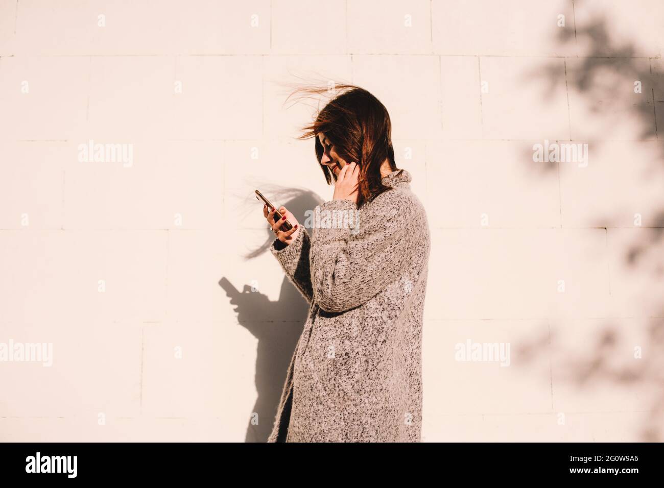 Vue latérale d'une femme heureuse utilisant un smartphone en se tenant contre le mur Banque D'Images