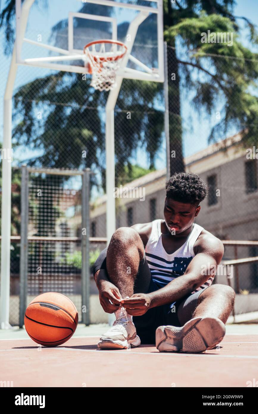 Portrait d'un garçon afro-américain noir portant ses lacets sur un terrain de basket urbain. Banque D'Images