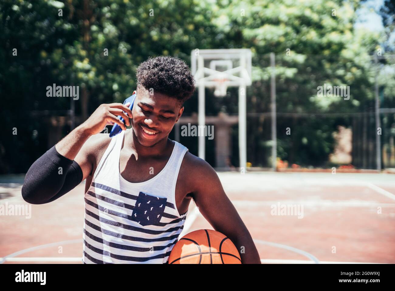 Portrait d'un garçon afro-américain noir parlant avec son téléphone portable sur un terrain de basket-ball urbain. Banque D'Images