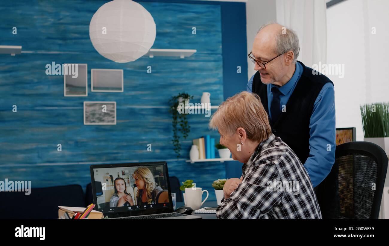 Une femme âgée excitée et son mari ayant une vidéoconférence sur ordinateur portable, parlant avec des neveux distants assis dans le salon. Appel en ligne avec la fille et la nièce en utilisant la communication moderne en ligne Banque D'Images