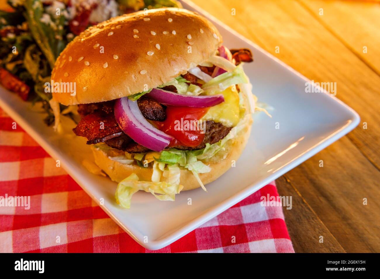 Cheeseburger de bœuf Angus recouvert de bacon croustillant servi avec une salade grecque Banque D'Images