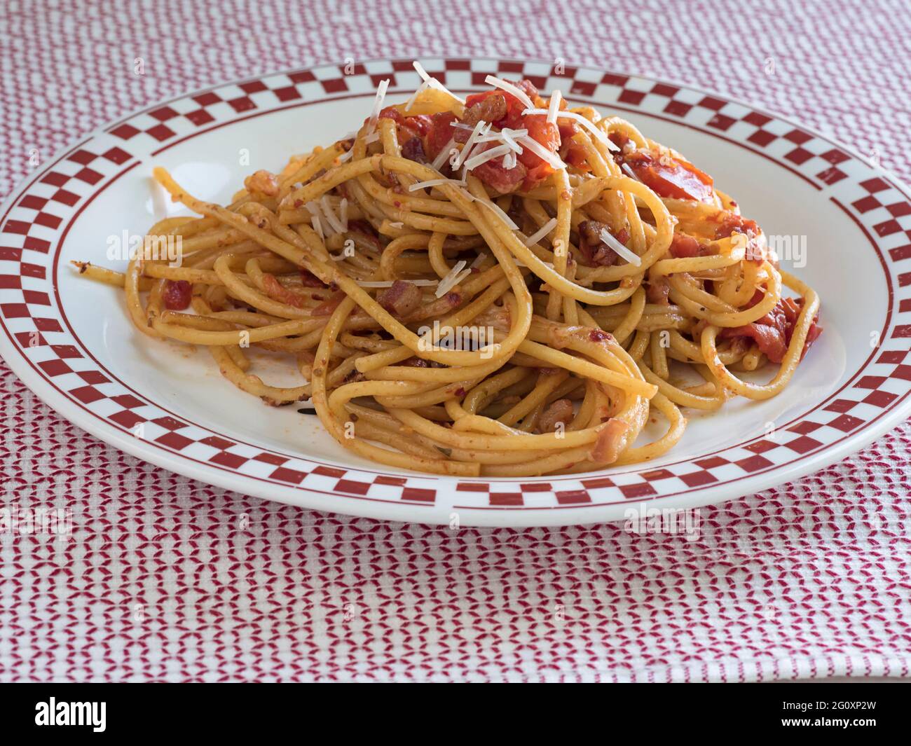 Un tas de Bucatini all'Amatriciana, un plat de pâtes italien à la pancetta et à la tomate, se trouve sur une assiette à carreaux, recouverte de parmesan Banque D'Images