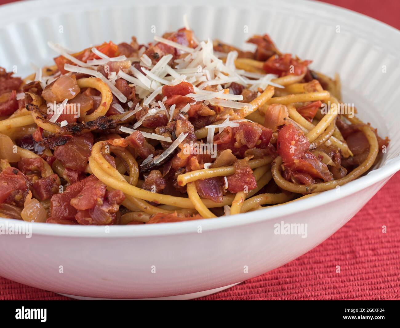 Un plat de service de Bucatini all'Amatriciana, un plat de pâtes italiennes avec pancetta et tomate, recouvert de parmesan, sur une table rouge Banque D'Images