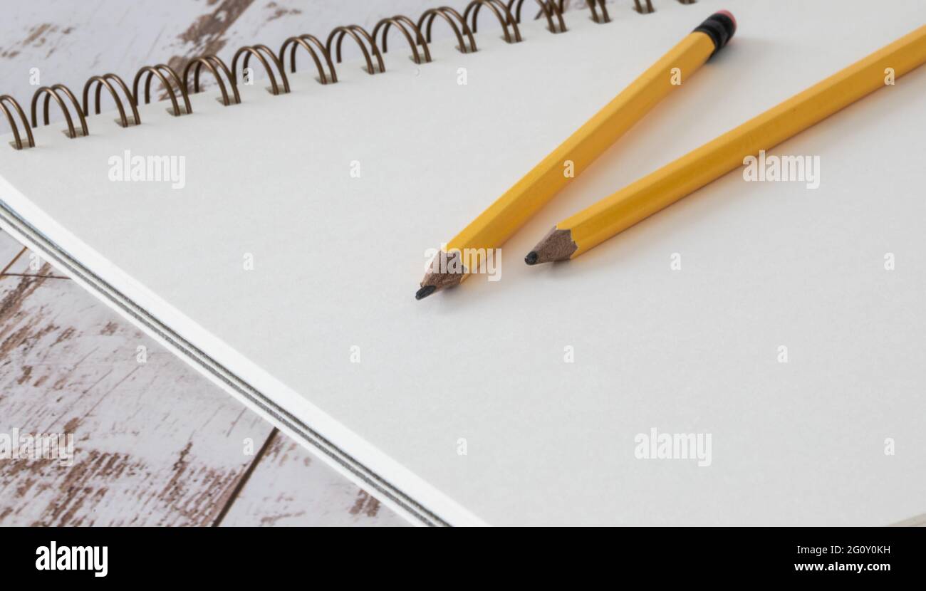 Carnet ouvert sur un papier blanc vierge avec des crayons jaunes sur une surface en bois Banque D'Images