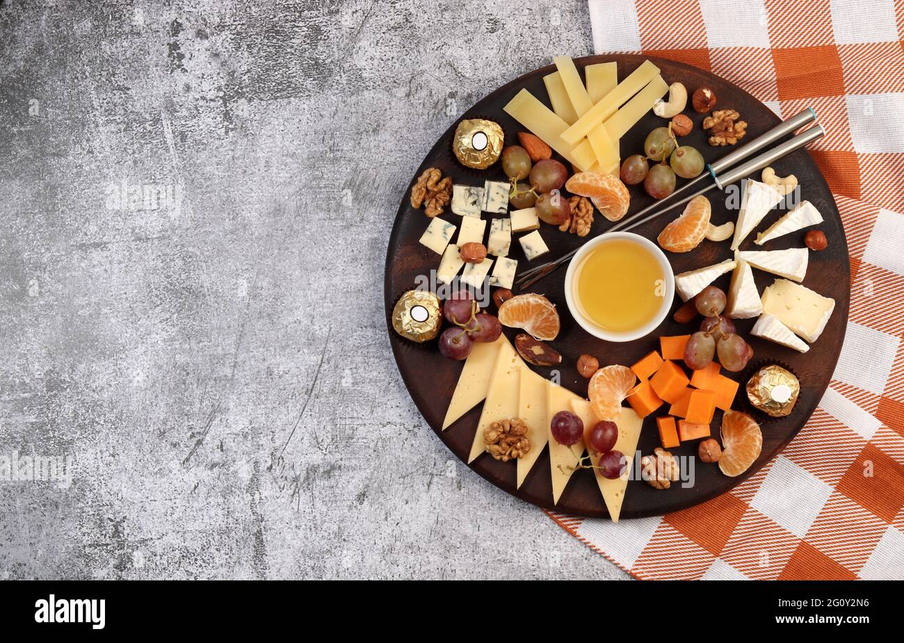 Plateau de fromages servi avec du miel, du raisin, des baies et des noix sur fond sombre. Vue de dessus, plan d'appartement Banque D'Images