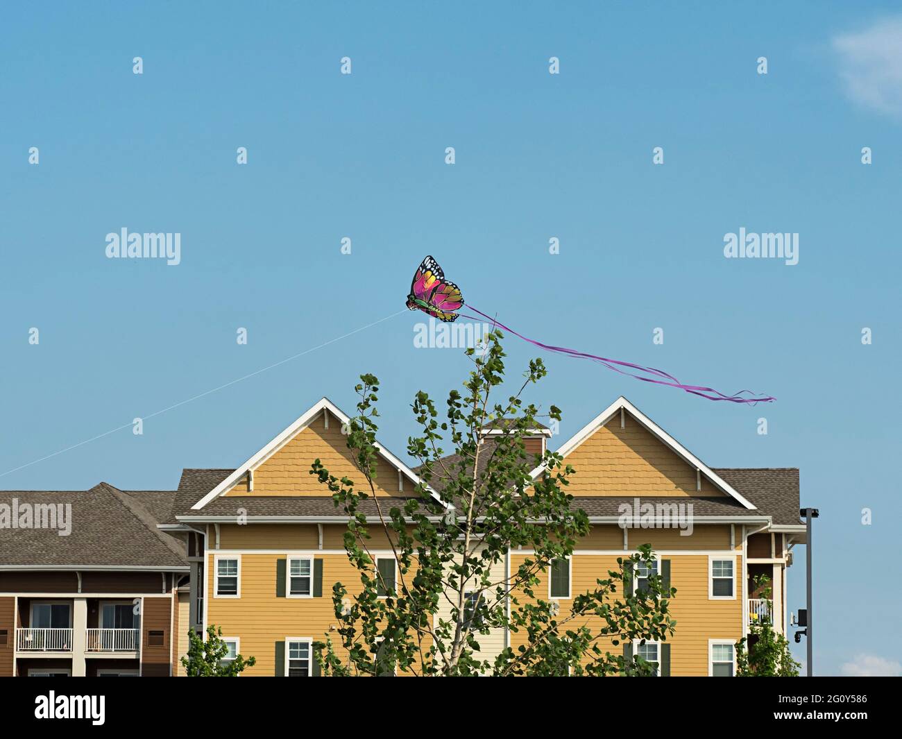 Un cerf-volant de papillon coloré survole un immeuble de résidence multifamilial non identifié dans un ciel presque sans nuages Banque D'Images