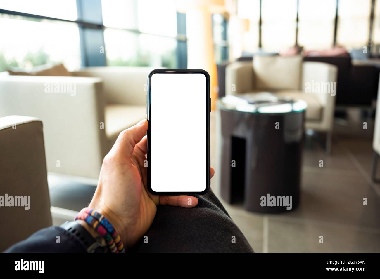 (Espace copie) vue en hauteur d'une main humaine tenant un smartphone avec un écran blanc dans un salon d'aéroport. Banque D'Images