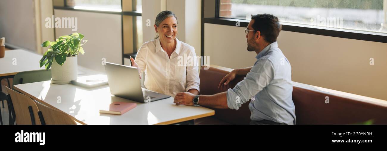 femme d'affaires cherchant heureux lors d'une réunion avec un collègue au bureau. Femme souriante pointant vers l'ordinateur portable et parlant avec un collègue au bureau. Banque D'Images