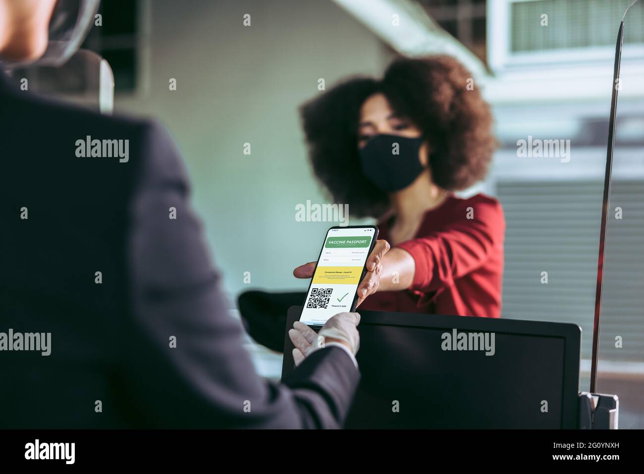 Femme portant un masque facial montrant son téléphone avec les détails de la vaccination Covid-19 à un préposé au sol au comptoir d'enregistrement de l'aéroport. Présence d'une femme Banque D'Images