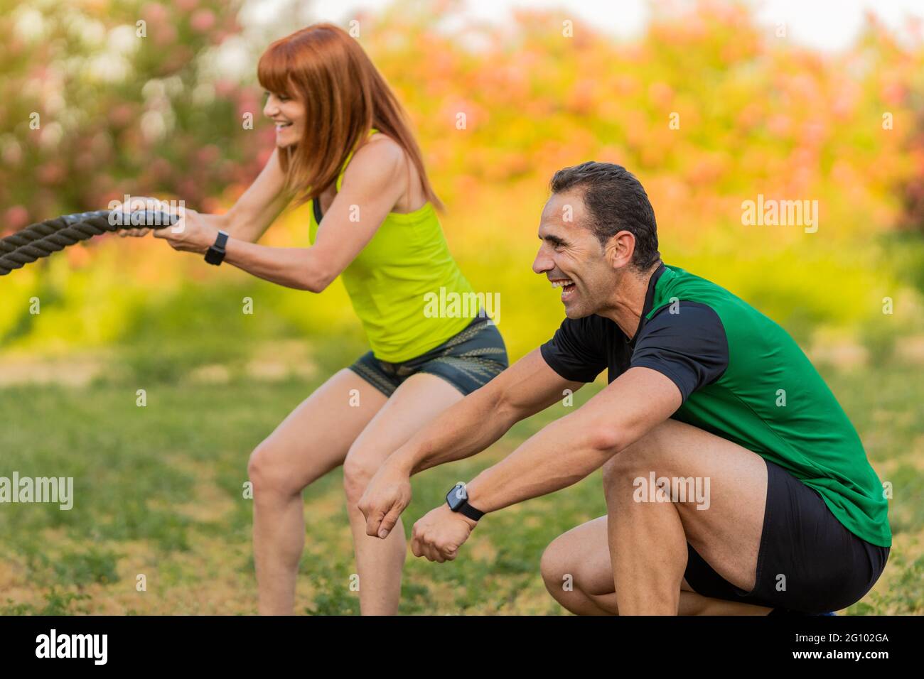 Entraînement d'entraîneur de fitness heureux avec une femme dans le parc et en utilisant un cordage de bataille. Banque D'Images