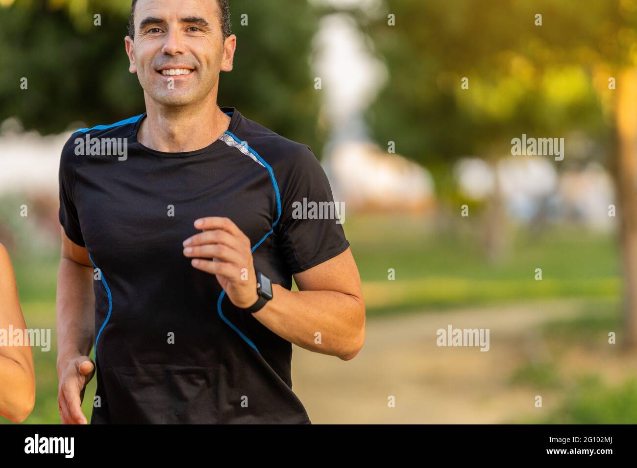 Joyeux homme adulte s'entraîner dans le parc et faire du jogging. Il sourit et regarde devant. Banque D'Images