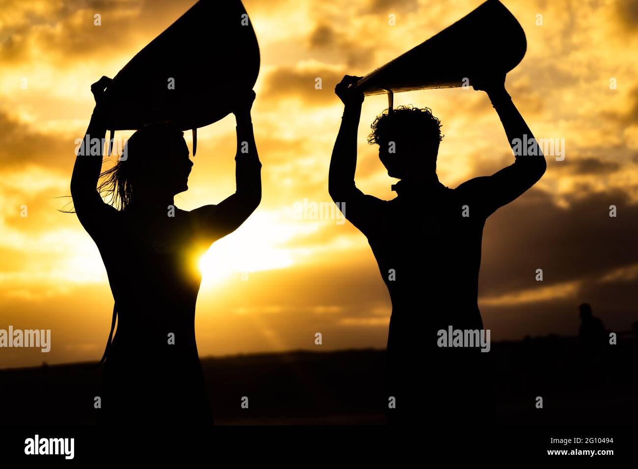 Silhouette des surfeurs transportant leurs planches de surf sur la plage du coucher du soleil. Sport et amitiés. Banque D'Images