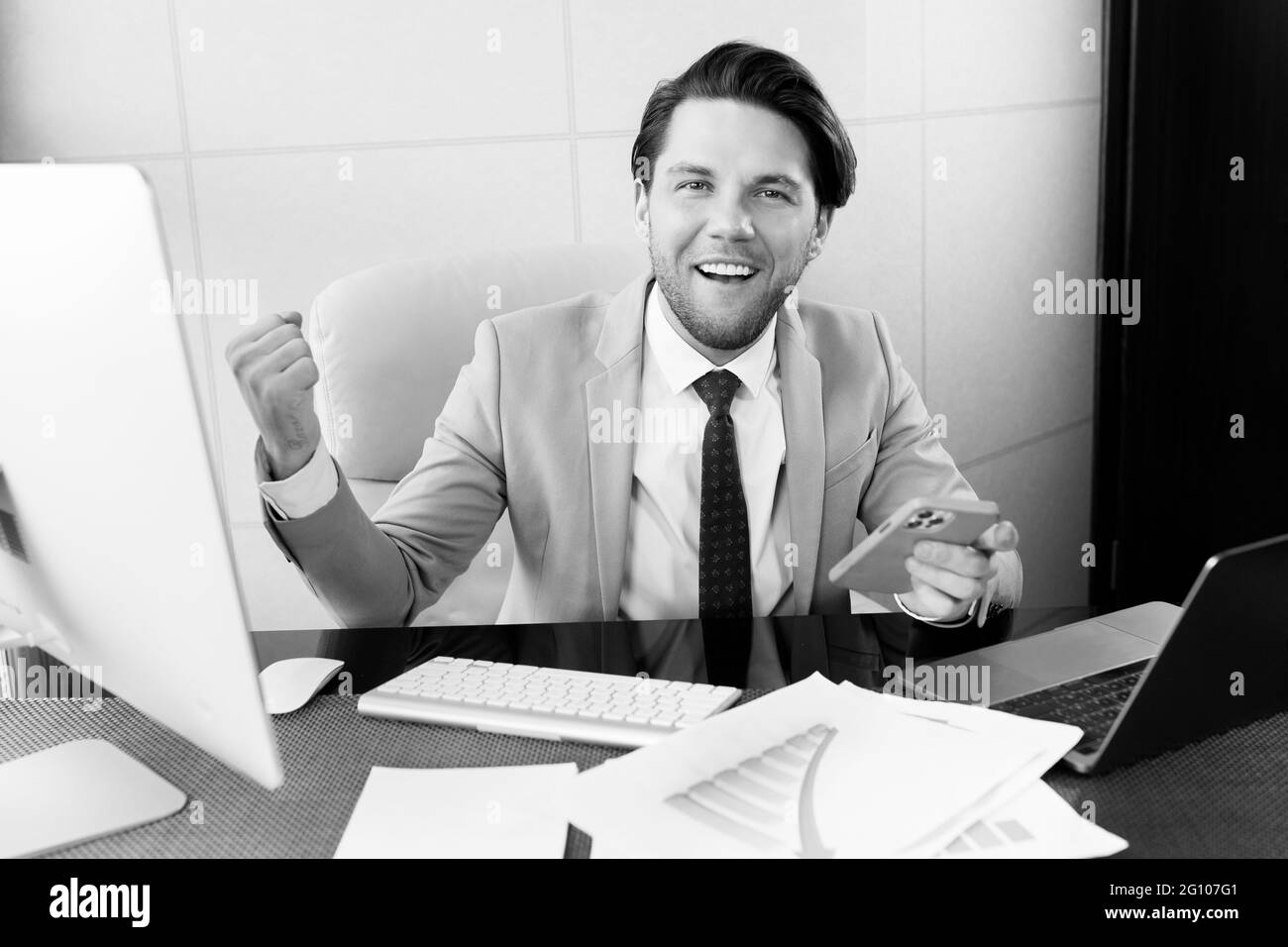 Portrait noir et blanc de l'homme d'affaires en costume regardant l'appareil photo, donner la motivation, homme professionnel réussi assis au bureau montrant poing Banque D'Images