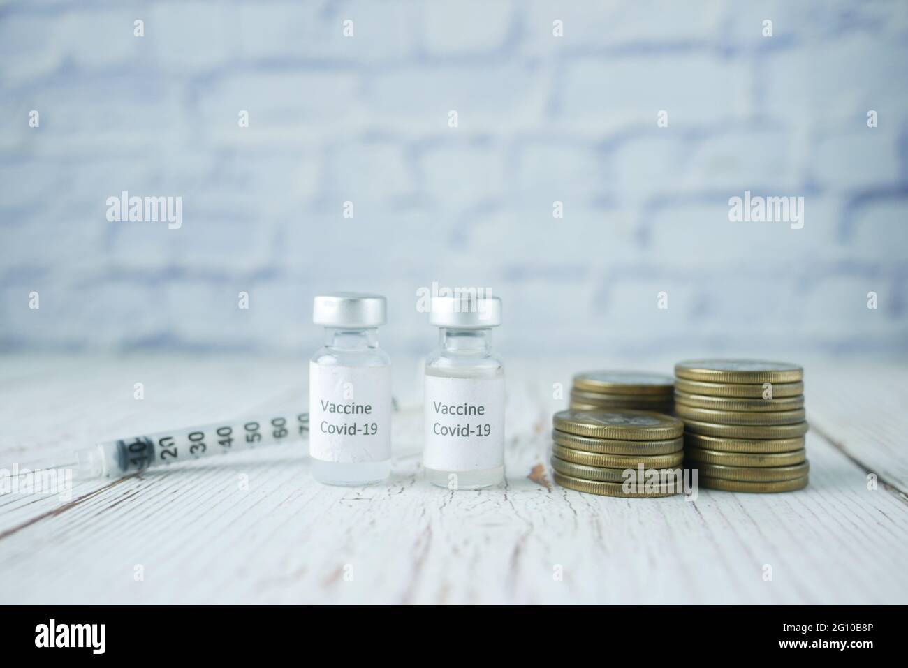 Concept de coût des soins de santé avec pile de pièces et vaccin corona sur table Banque D'Images