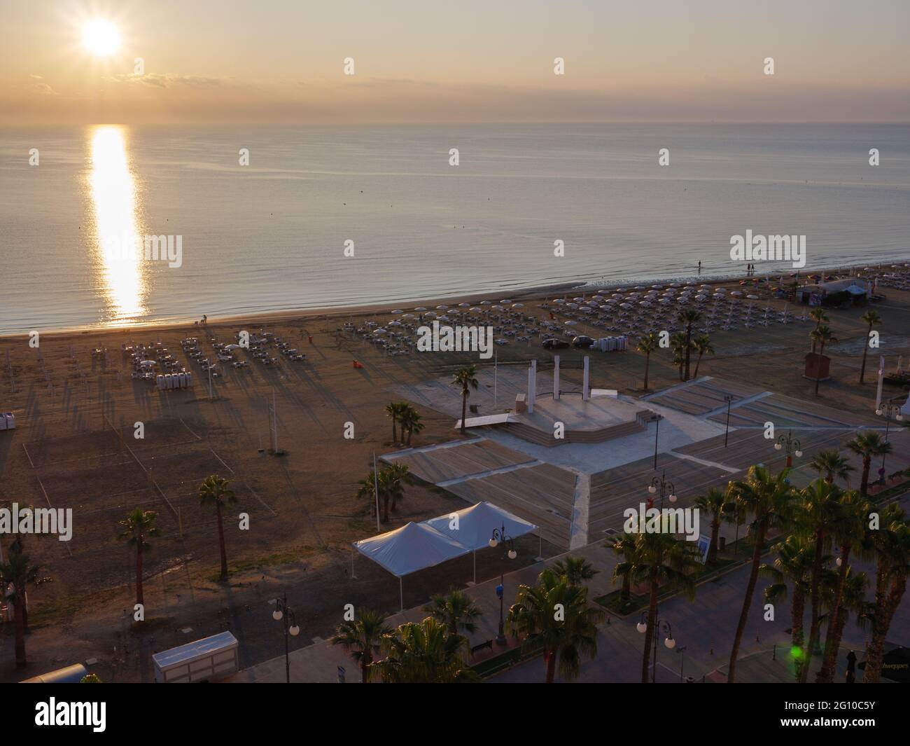 Vue aérienne du dessus surplombant le soleil se levant sur la mer Méditerranée calme avec le chemin du soleil sur la surface de l'eau. Chaises longues avec parasols, terrain de volley. Banque D'Images