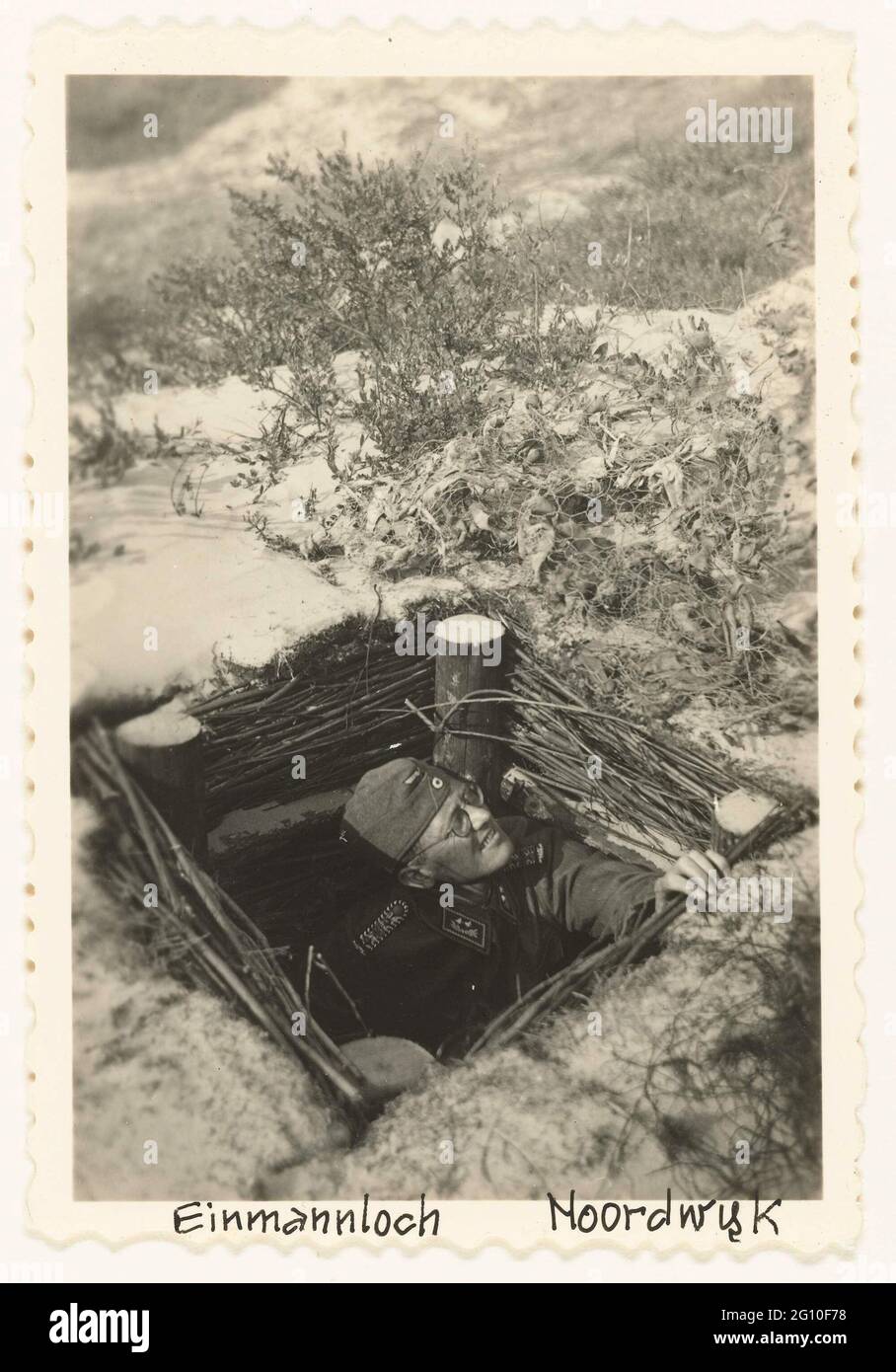 Soldat allemand dans 'Einmannloch'. Un soldat allemand regarde d'un 'ëinmannloch' (puits de tir) dans les dunes de Noordwijk en hiver, il y a de la neige. Banque D'Images