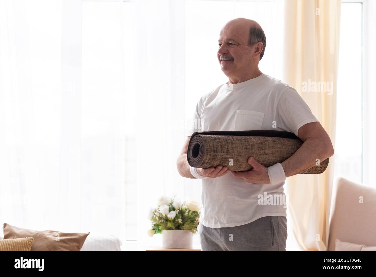 Homme senior avec un tapis de yoga regardant la caméra avec le sourire Banque D'Images