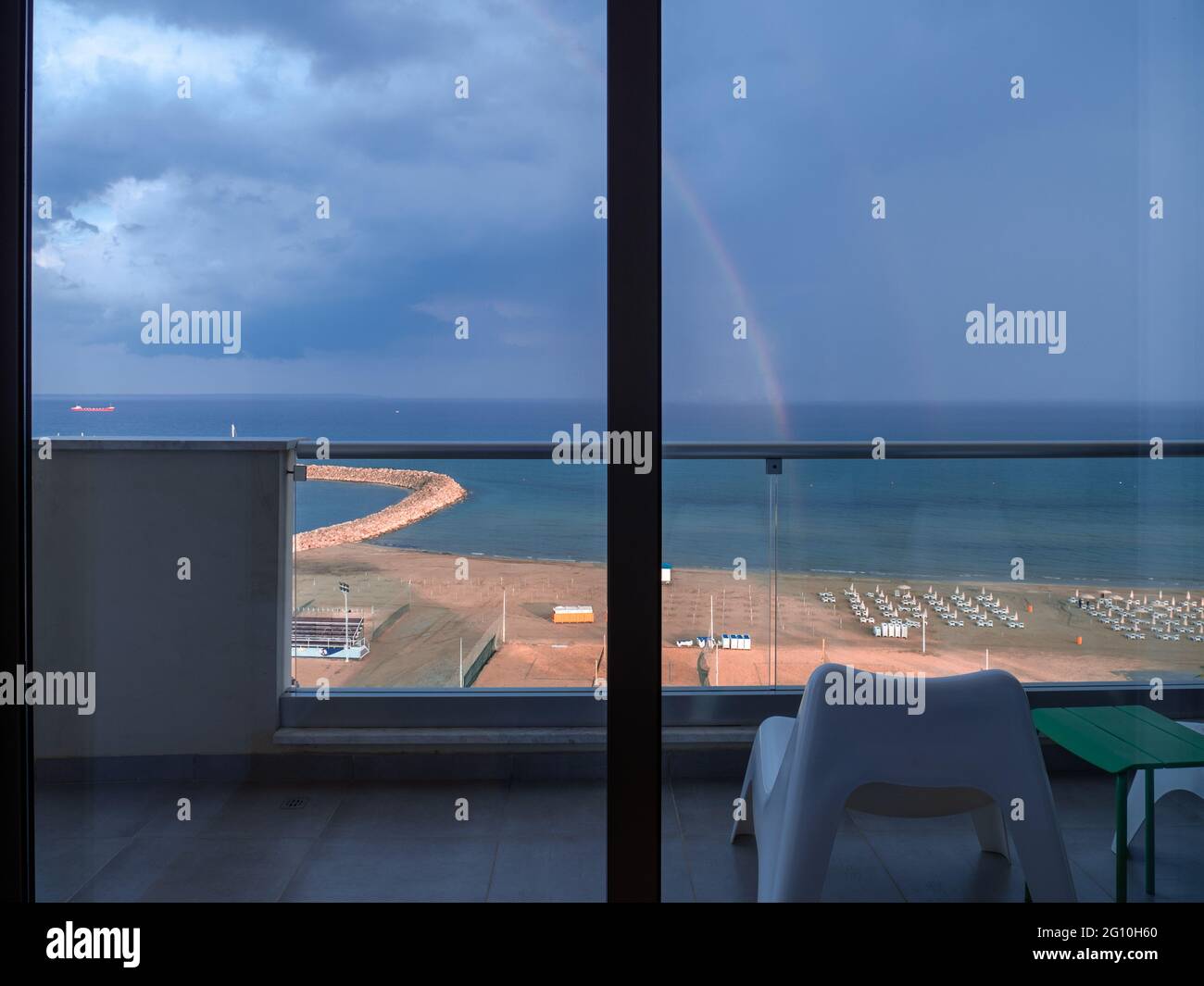 Vue aérienne supérieure surplombant l'arc-en-ciel au-dessus de la plage méditerranéenne avec chaises longues près de la promenade des palmiers de Finikoudes dans la ville de Larnaca. Ciel sombre et nuageux. Banque D'Images